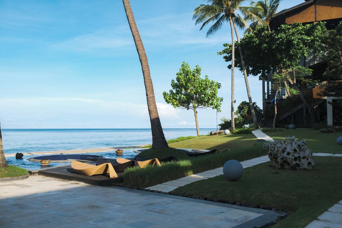 A resort with a pool area, lounge chairs, palm trees, and a view of the ocean.