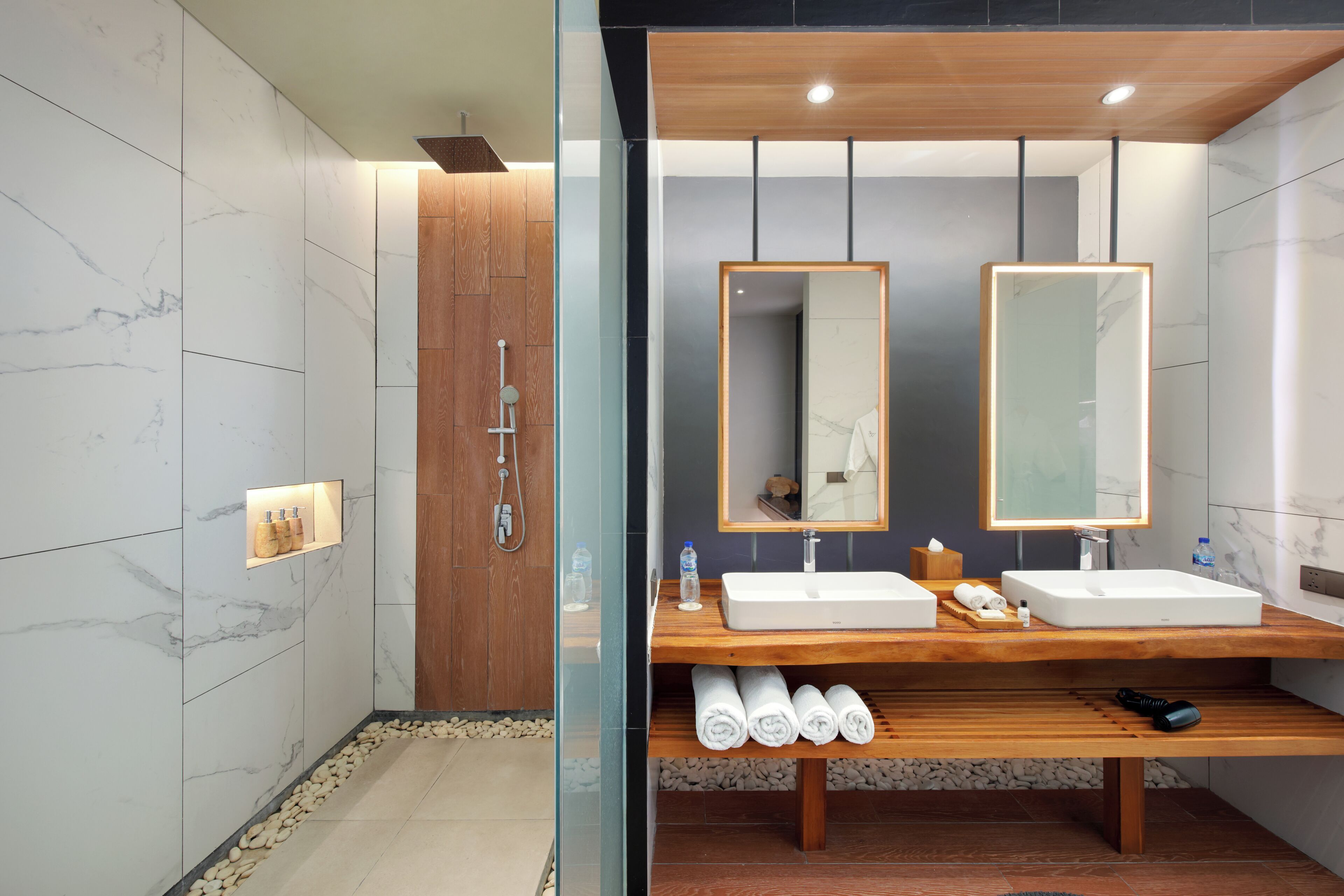 A modern bathroom with two sinks, a wooden vanity, a large mirror, and a shower area.