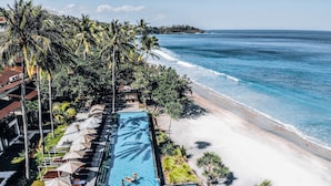 A rectangular swimming pool adjacent to a beach, surrounded by palm trees and lounge chairs. - Katamaran Hotel & Resort Lombok (Senggigi)
