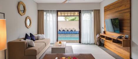 A modern hotel room with a sofa, coffee table, TV, and a view of a pool.