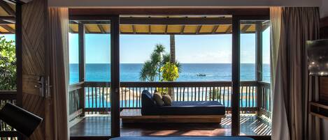 A room with a large window, a bed, a wooden desk, and a view of the ocean.