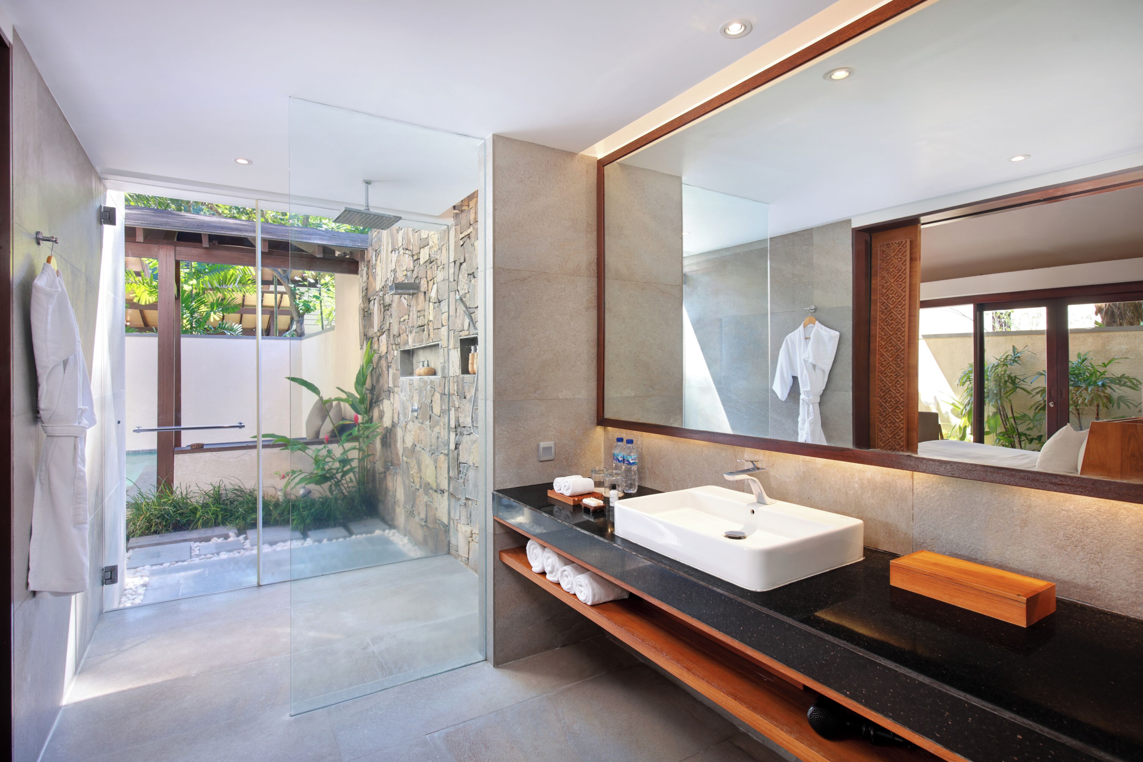 Un baño moderno con cabina de ducha de vidrio, un espejo grande y un mostrador negro con lavamanos blanco.