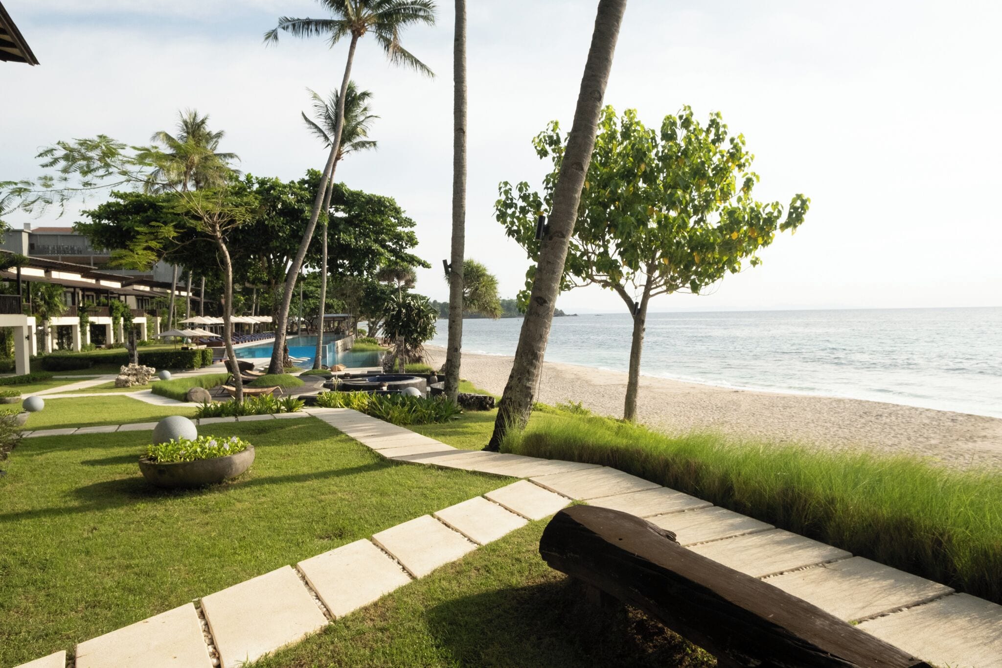 Un resort con piscina, palmeras, playa y una vista despejada del océano.