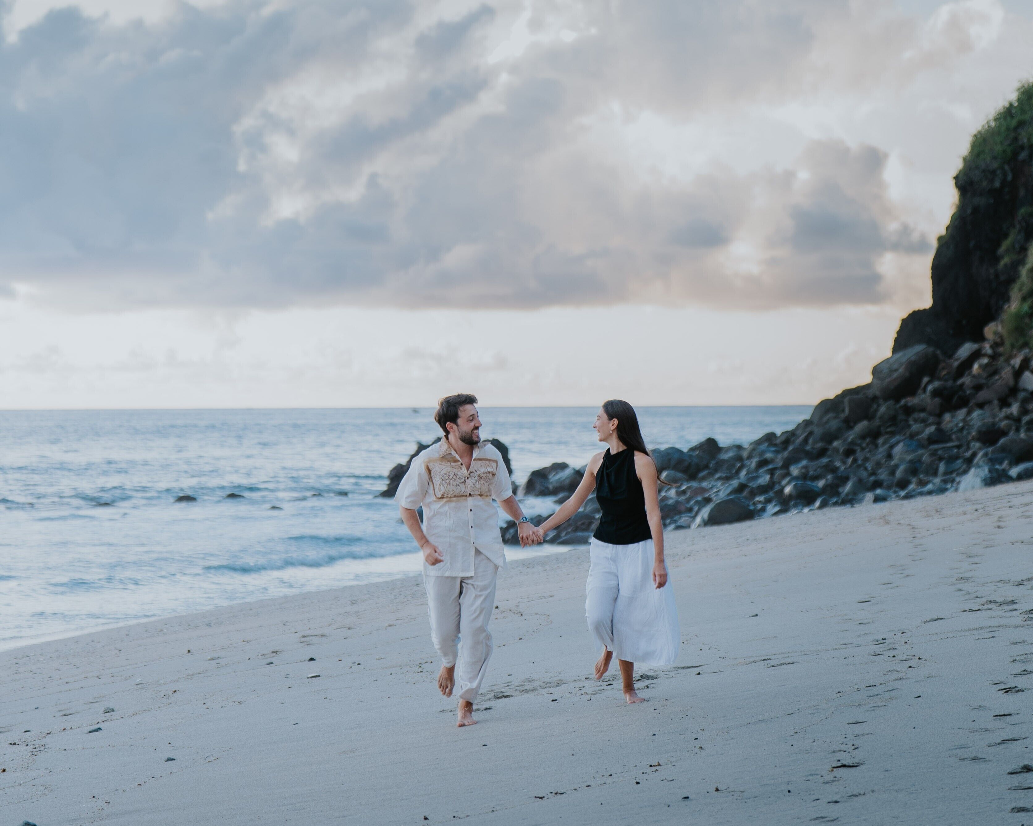 Una pareja camina por la playa con un acantilado rocoso al fondo.