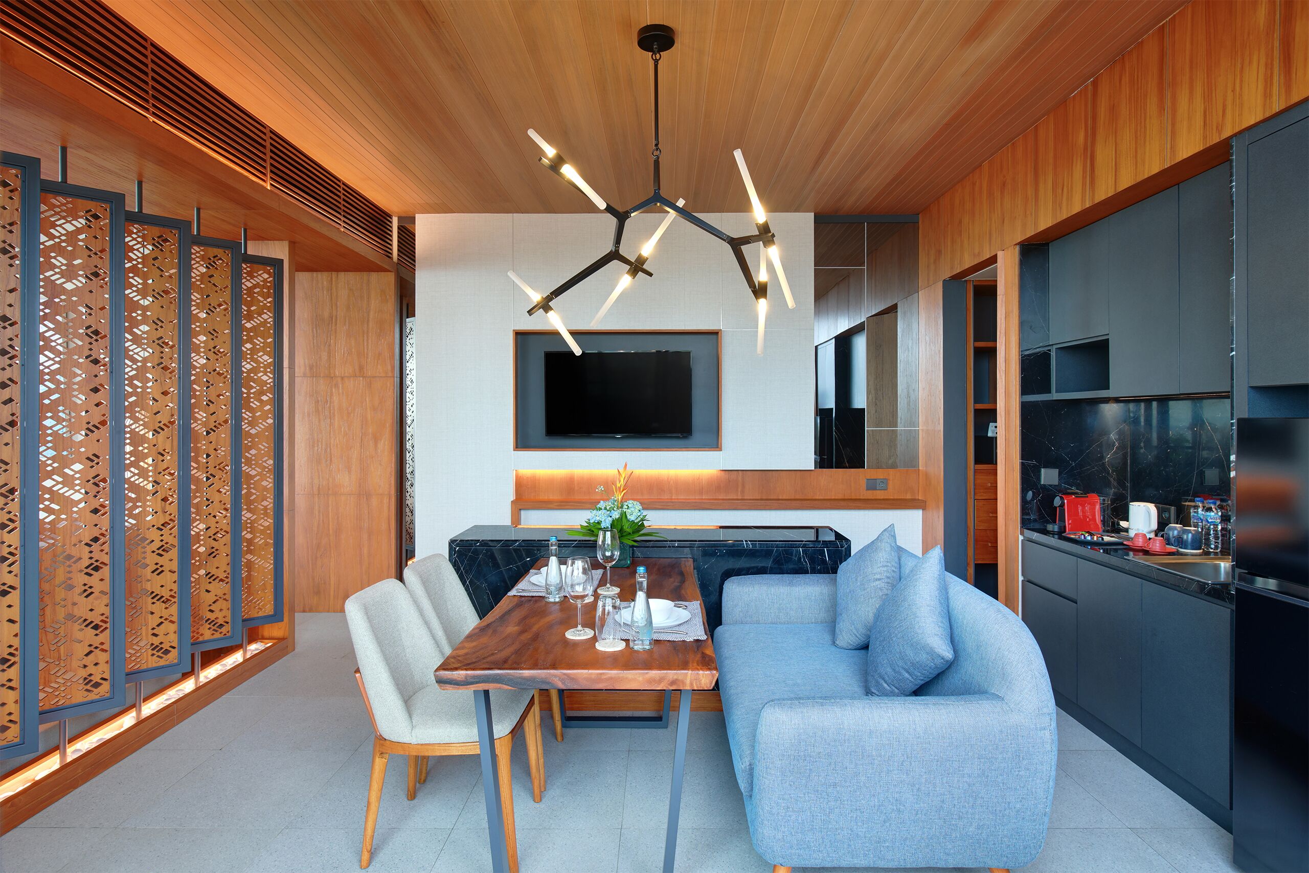 A modern kitchen with a built-in stove, a dining area with a wooden table and chairs, and a blue sofa.