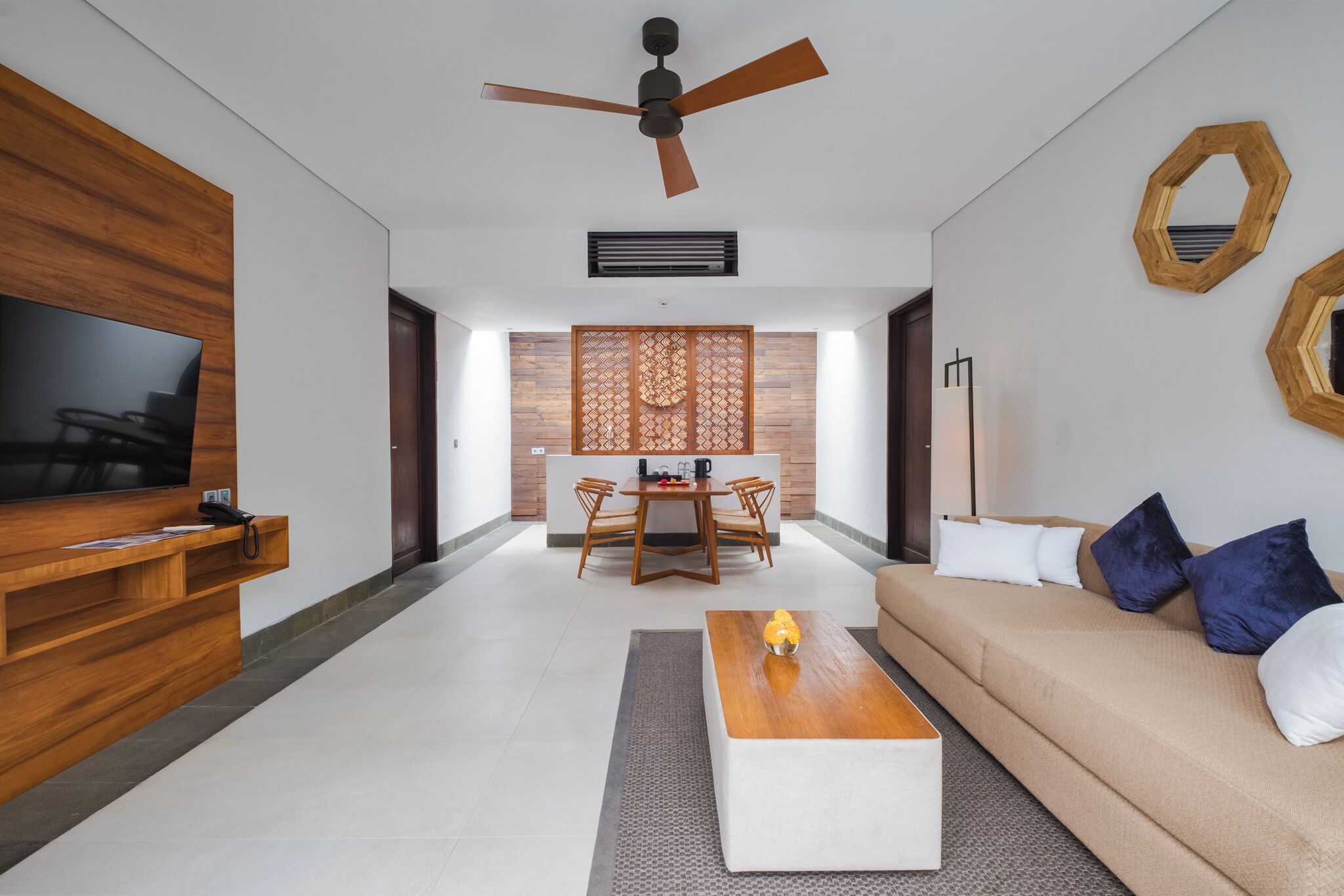 A modern living room with a flat-screen TV, wooden furniture, a ceiling fan, and a dining area with a wooden partition.