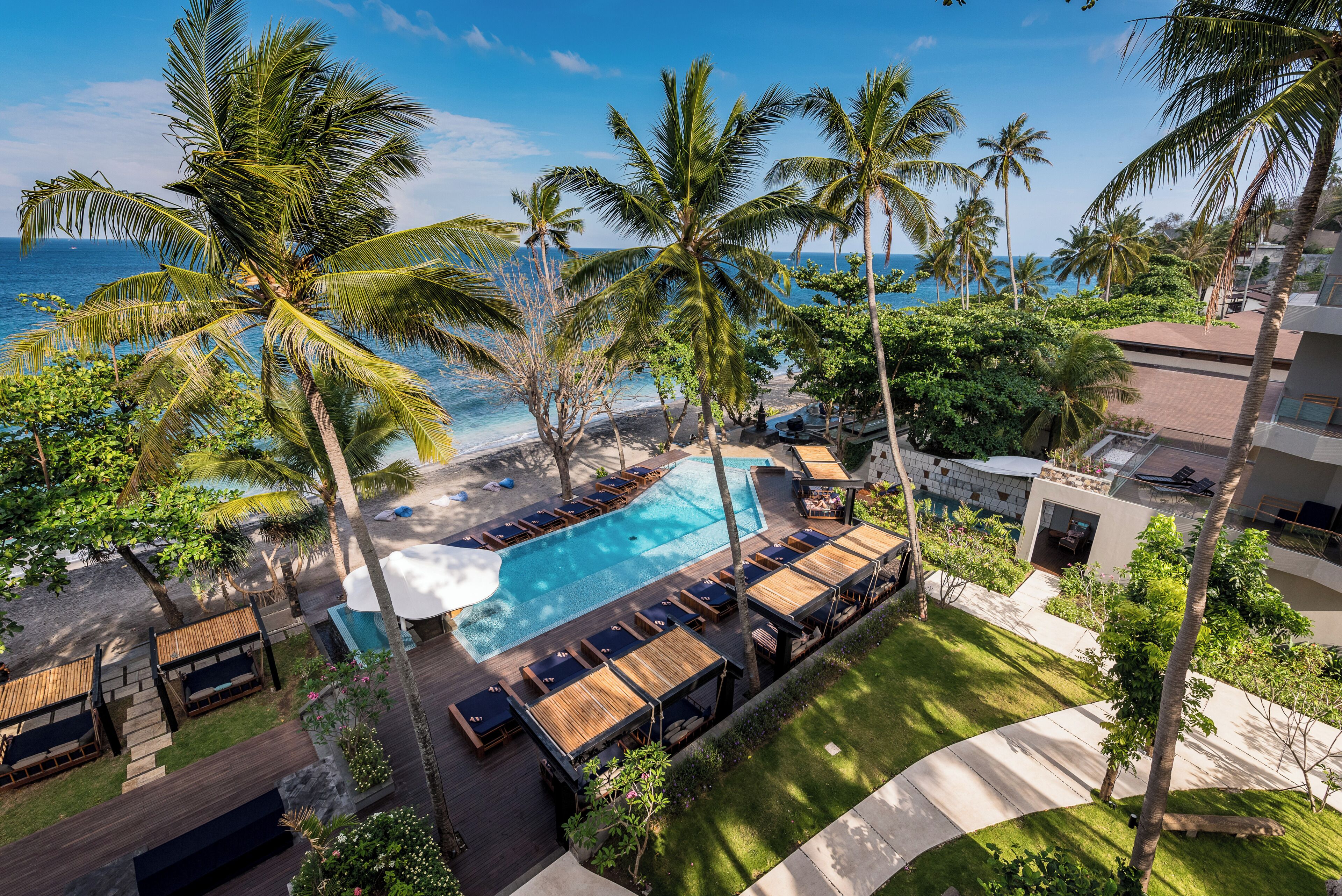 A resort with a swimming pool surrounded by lounge chairs, palm trees, and a view of the ocean.