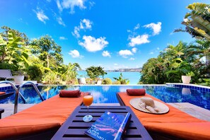 A poolside lounge with orange cushions, a glass of orange juice, and a magazine titled "Life Less Ordinary." - Villa Seven Swifts (Koh Samui)