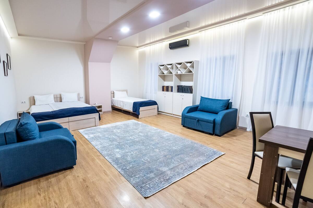 Una habitación de hotel moderna con cama, dos sofás, una mesa de comedor y un armario empotrado.