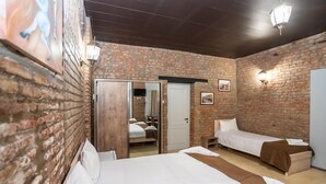 A room with brick walls, two beds, a wooden door, and a mirror. - Hotel Tiflis (Tbilisi)