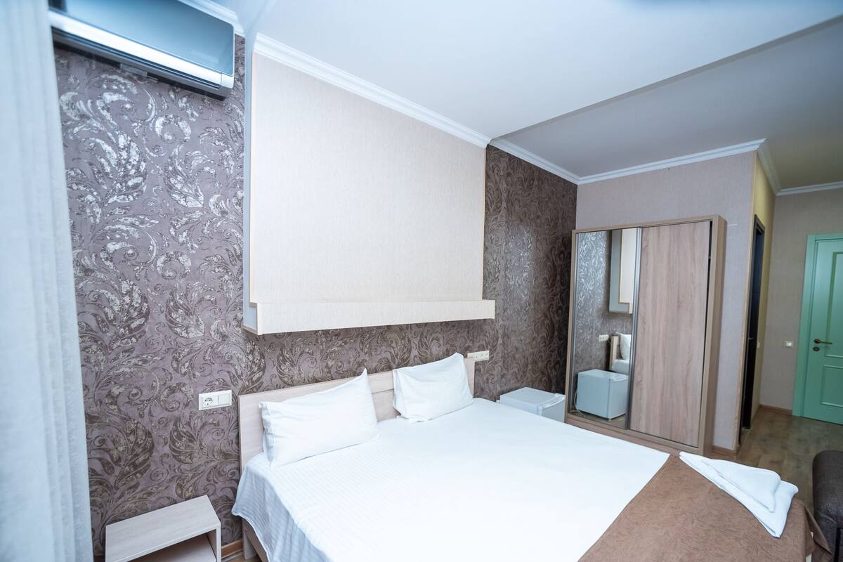 Una habitación de hotel con una cama grande, una mesita de noche, un espejo y un armario.
