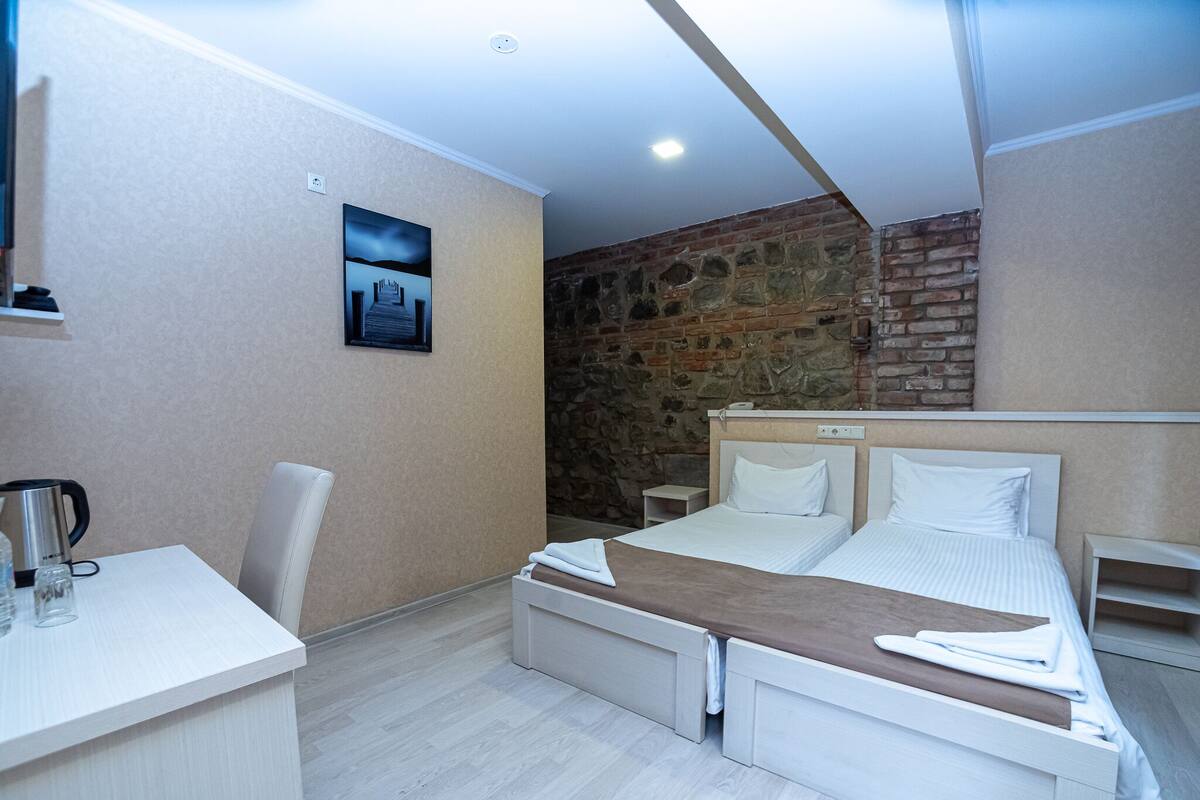 Una habitación de hotel moderna con cama, mesitas de noche, escritorio y una pared decorativa de piedra.