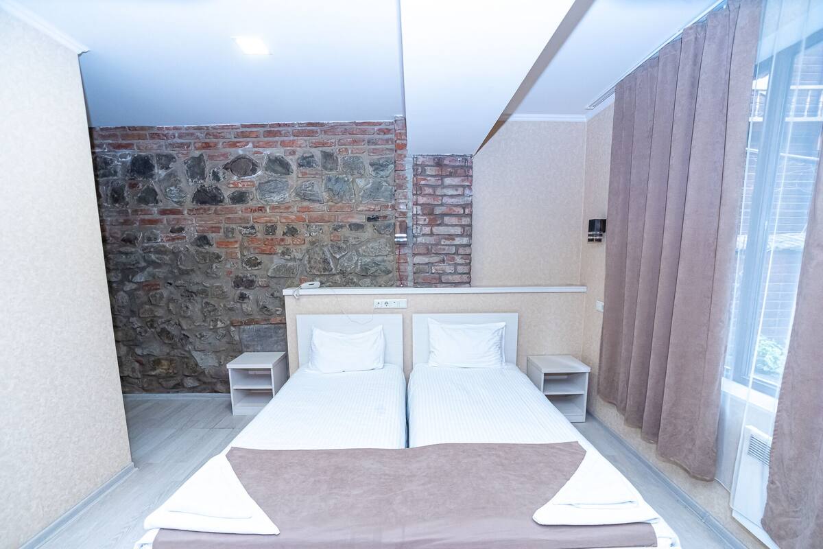 Un dormitorio con pared de piedra, cama con ropa blanca y ventana con cortinas.