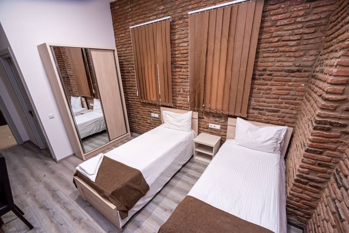 Un dormitorio con dos camas, un espejo y una pared de ladrillo.