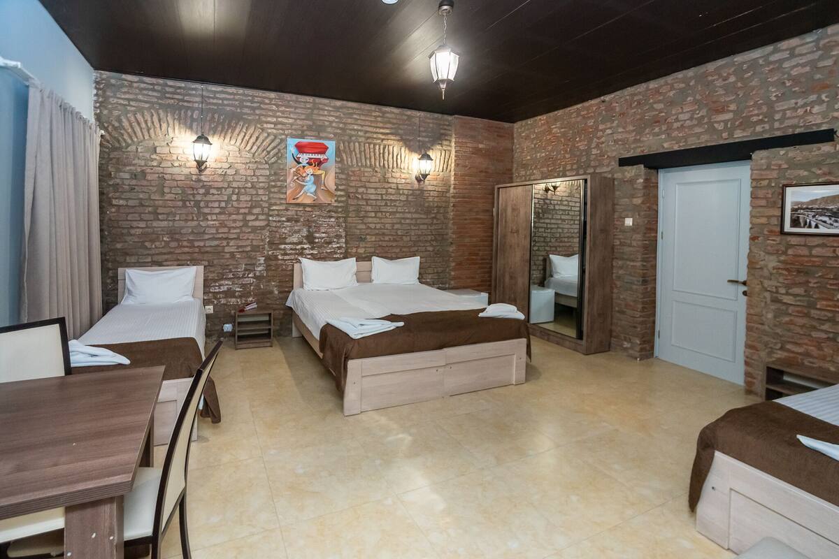 Una habitación de hotel con pared de ladrillo, una cama, un escritorio y un armario.