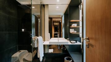 Un baño moderno con ducha envuelta en vidrio, un lavamanos blanco y un mueble de tocador de madera.