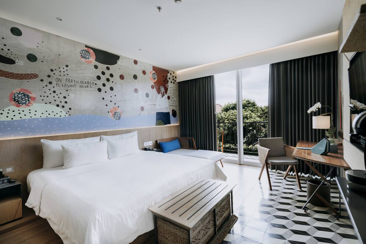 A modern hotel room with a large bed, a desk, and a view of the outdoors.