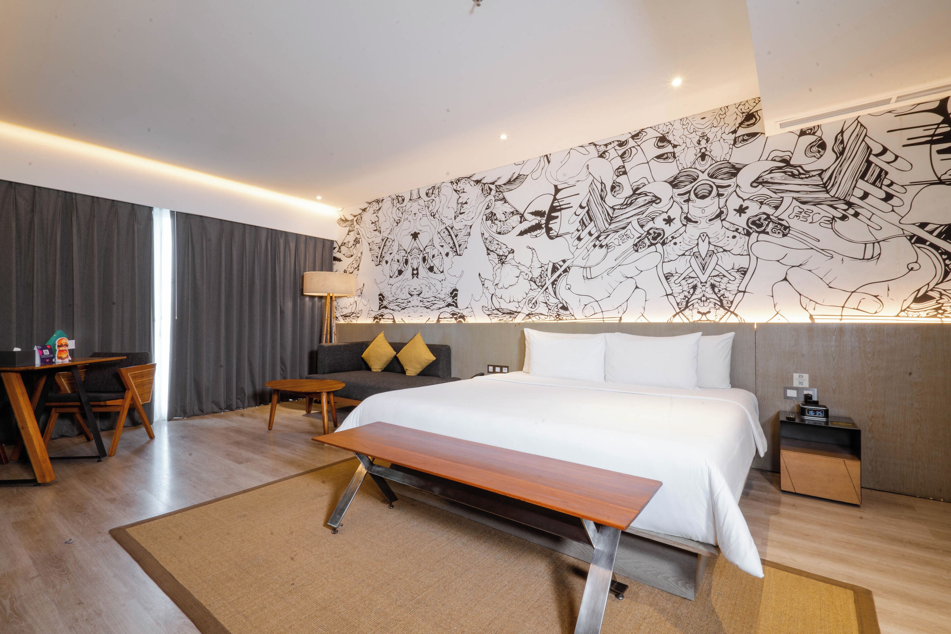 Ett modernt hotellrum med en stor säng, ett skrivbord, en soffa och en väggmålning.