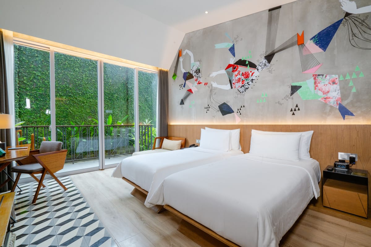 A hotel room with two beds, a large window, a geometric patterned rug, and a wall art piece.
