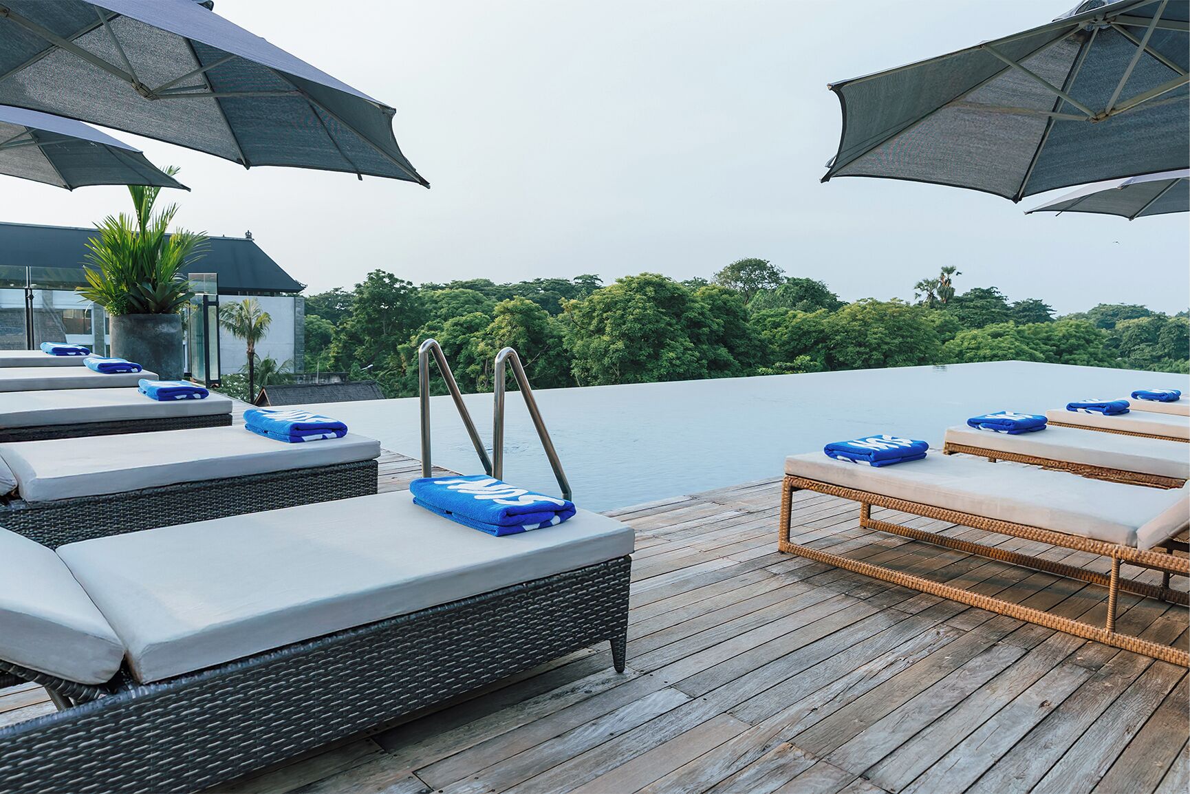 A rooftop pool area with lounge chairs and umbrellas, overlooking a body of water and greenery.