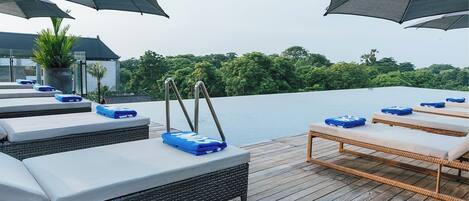 A rooftop pool area with lounge chairs and umbrellas, overlooking a body of water and greenery.