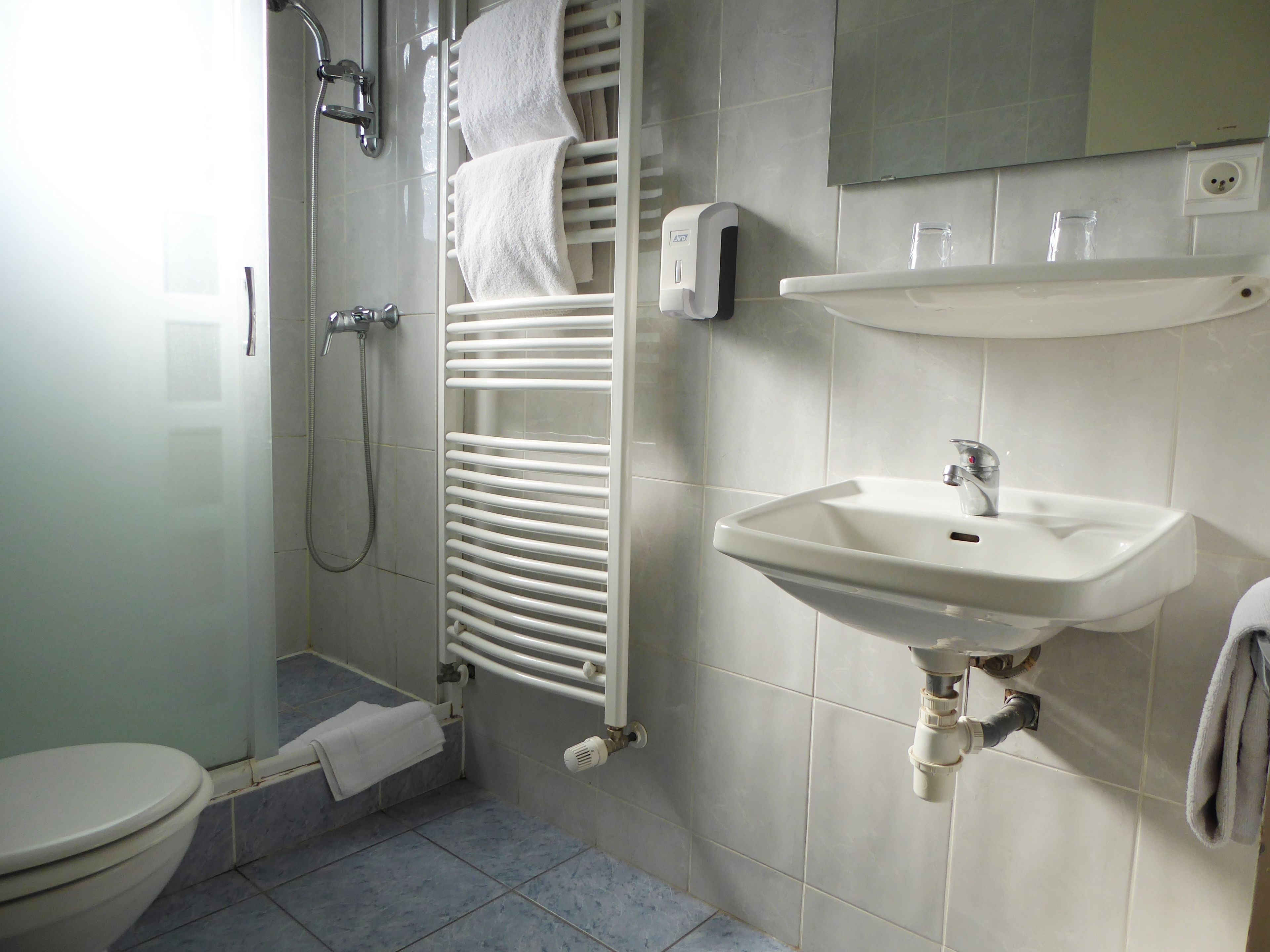 A bathroom with a toilet, shower, towel rack, sink, and a mirror.