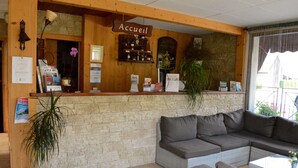 Un área de recepción con mostrador de madera, un cartel que dice 'Accueil' y una zona de estar con sofá y sillones.