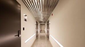 Un pasillo largo y estrecho con puertas a ambos lados, suelo de tonos claros y techo con luminarias lineales.