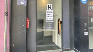 La entrada al Grand Hotel Myongdong 4, con mostrador de recepción, detector de incendios y un cartel con el horario de check-in.
