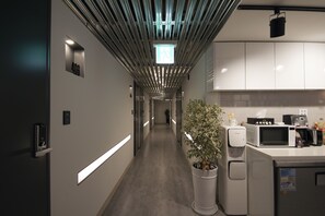 A modern hotel corridor with a long hallway, a potted plant, a microwave, and a coffee machine.