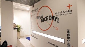 Una pared con el mensaje '¡Que tenga un buen día!' en varios idiomas y un símbolo de cruz.