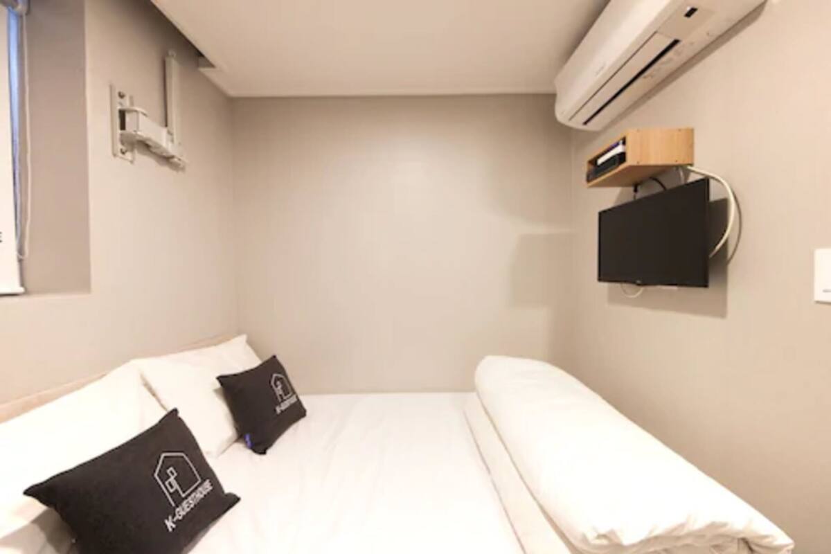Une petite chambre d’hôtel moderne, équipée d’un lit, d’un téléviseur fixé au mur et d’un appareil de climatisation.