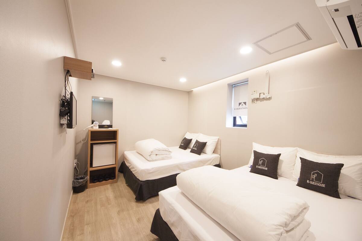 Une chambre d’hôtel avec deux lits, un petit bureau, un miroir et une fenêtre.