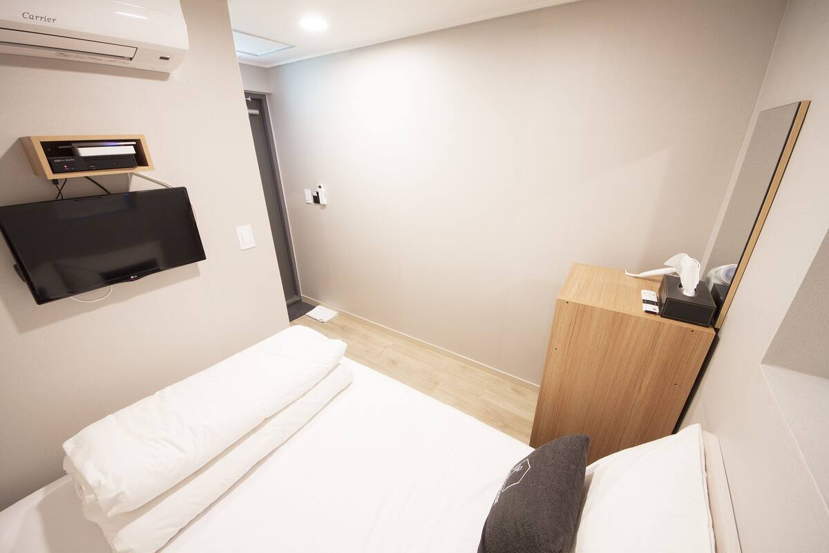 Une chambre d’hôtel avec un lit, un téléviseur fixé au mur, une table de chevet en bois et un miroir.