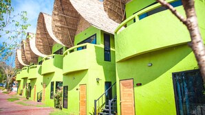 A row of bright green buildings with thatched roofs and wooden doors. - Reewa Waree Resort (Pak Chong)