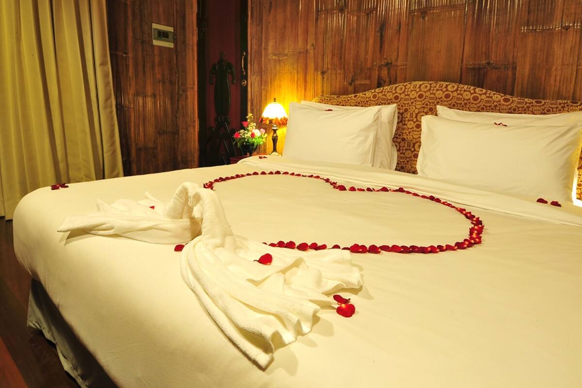 Une chambre d’hôtel avec un grand lit, une tête de lit en bois et une table de chevet avec une lampe et des fleurs.