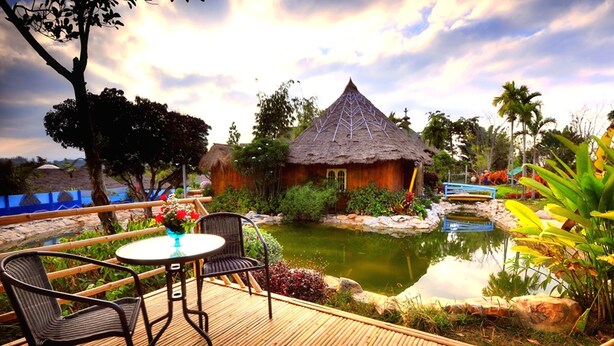 A wooden deck with a table and chairs, a thatched-roof hut, and a pond with surrounding vegetation. - Reewa Waree Resort (Pak Chong)