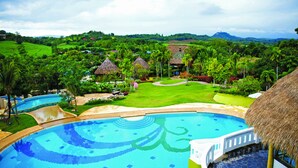 A resort with a large swimming pool, lush greenery, and thatched-roof buildings. - Reewa Waree Resort (Pak Chong)