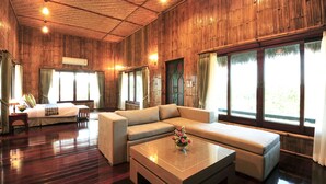 A spacious room with a large sectional sofa, a coffee table with a vase, and a bed with a nightstand. - Reewa Waree Resort (Pak Chong)
