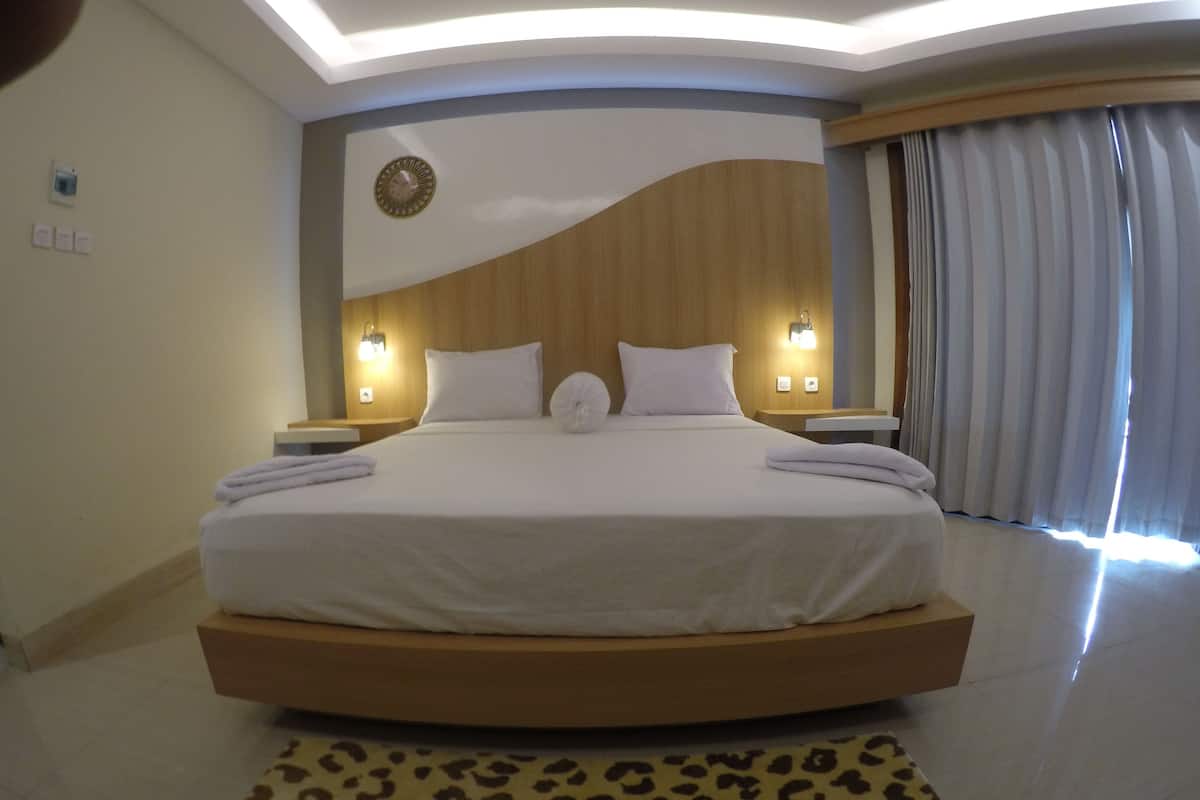 Una habitació d'hotel moderna amb un llit gran, dues taules de nit, un rellotge a la paret i una finestra amb cortines.
