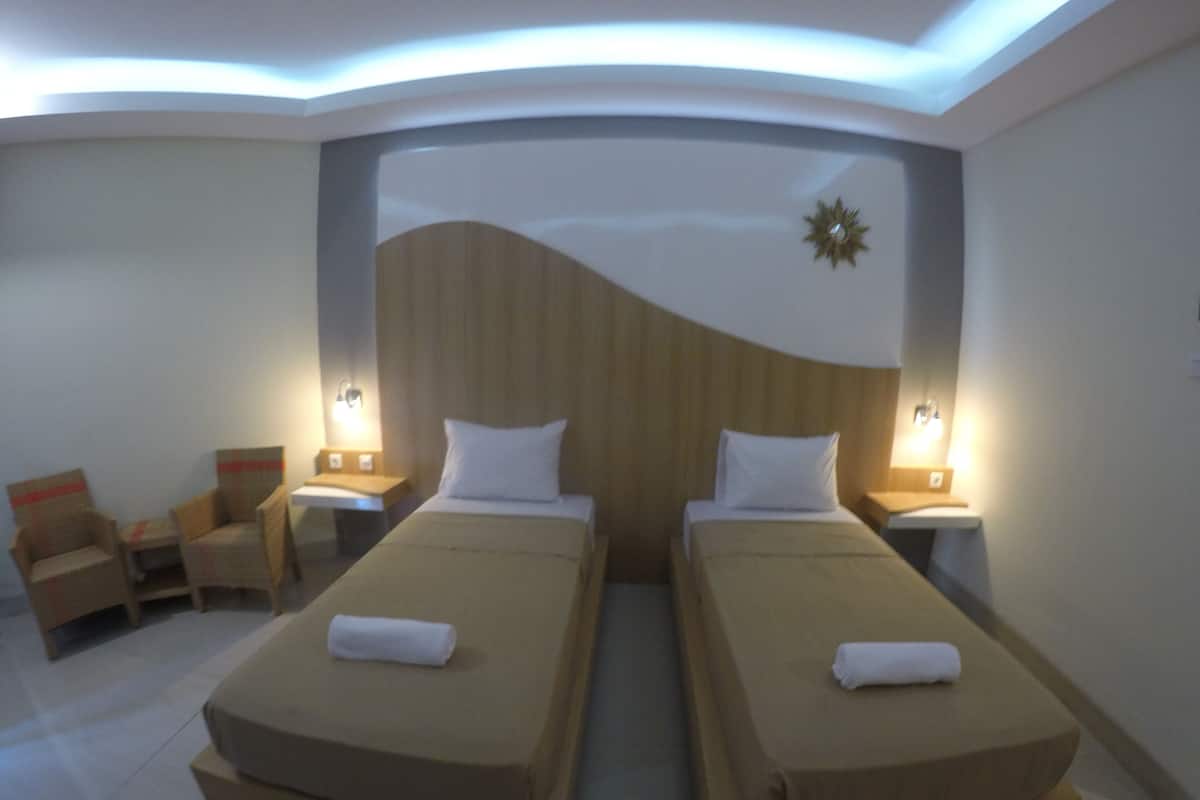 Habitació d'hotel amb dos llits, una petita zona de seients amb cadires i un panell decoratiu a la paret.