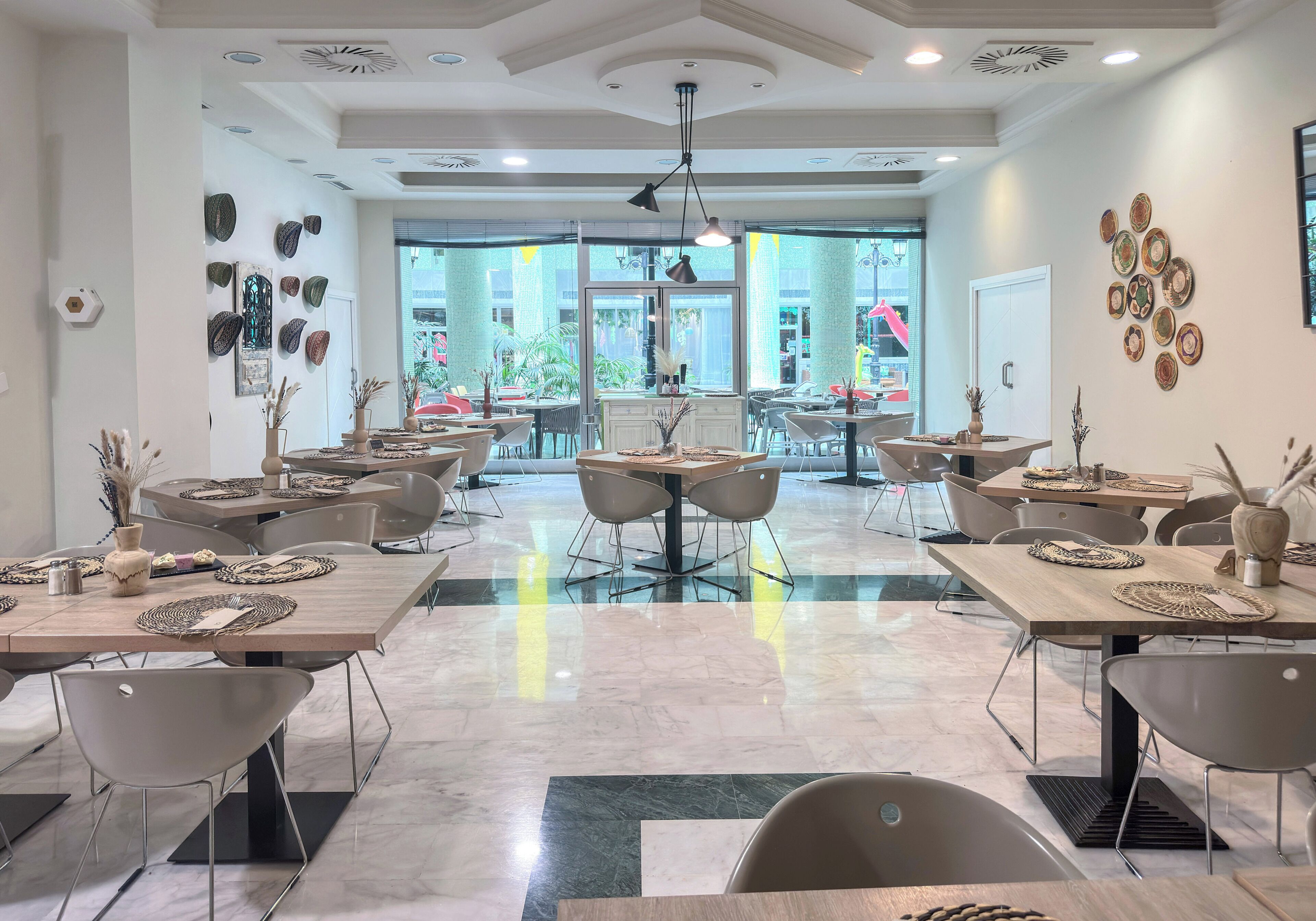A spacious dining area with multiple tables and chairs, large windows, and a modern ceiling design.