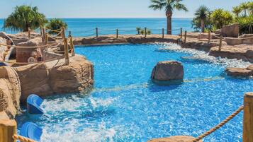 A pool with clear blue water, surrounded by rocks and palm trees.