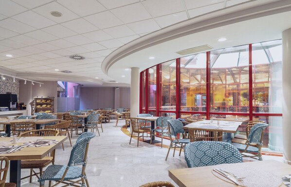 A spacious indoor dining area with multiple tables and chairs, a large glass window, and a modern ceiling design.