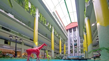 En inomhuspool med dinosaurieskulpturer, flera våningar och ett högt tak med naturligt ljusinsläpp.
