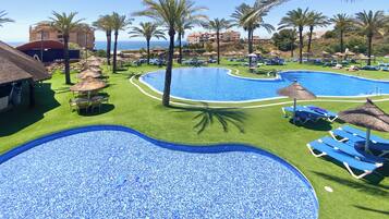 A resort pool area with multiple pools, palm trees, and lounge chairs.