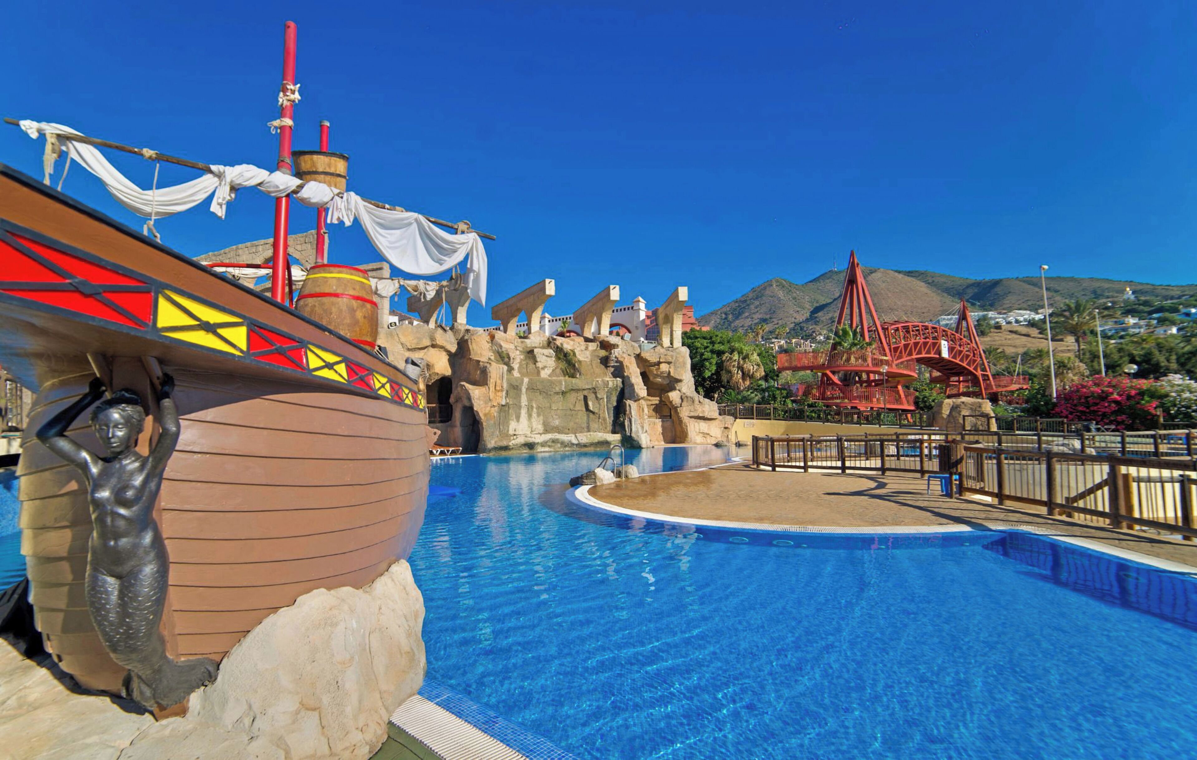 Une piscine dont le décor est inspiré des bateaux, avec un pont et un paysage montagneux en arrière-plan.
