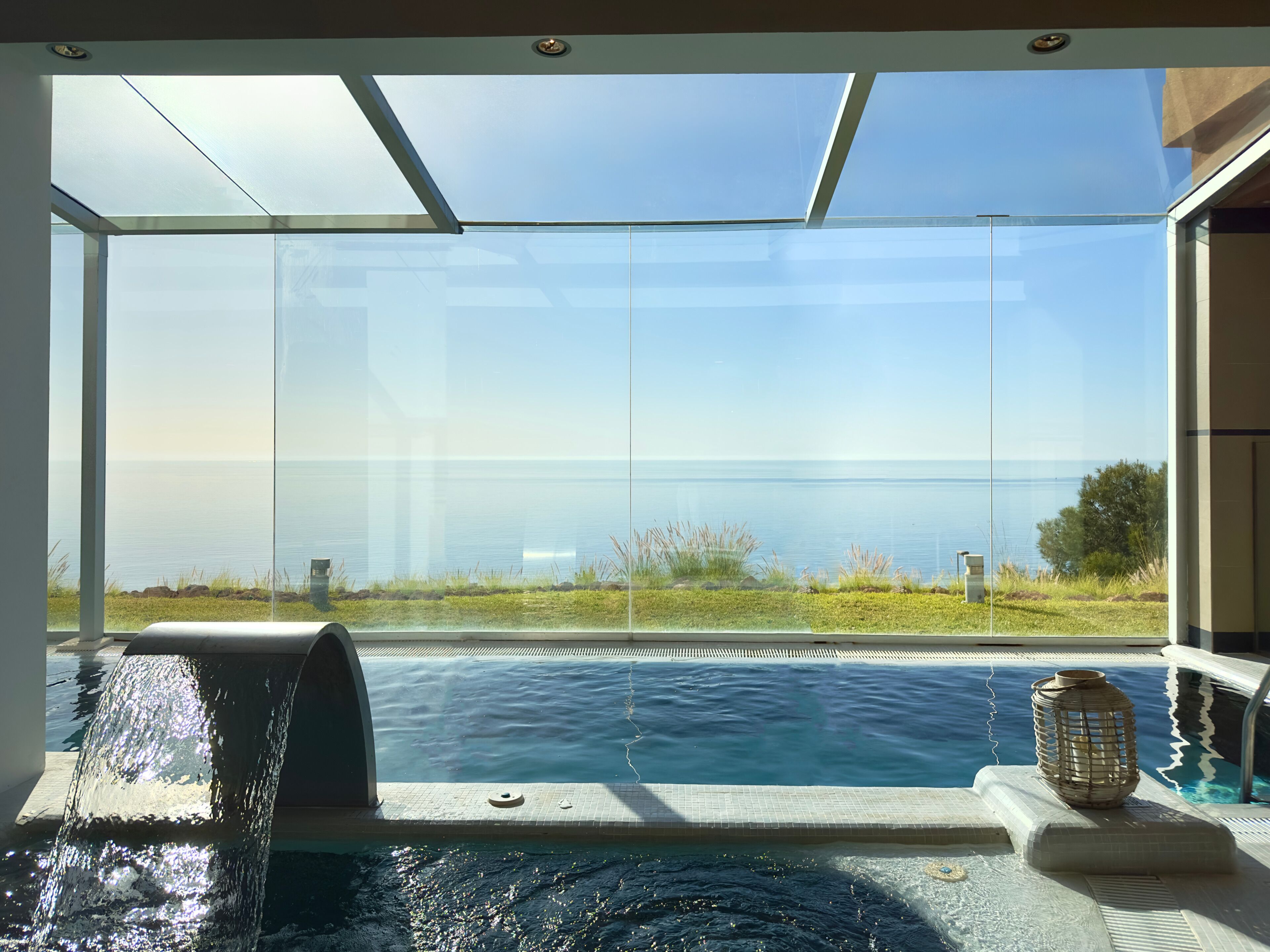 Ein moderner Pool mit Wasserspiel, klaren Glaswänden und Meerblick.