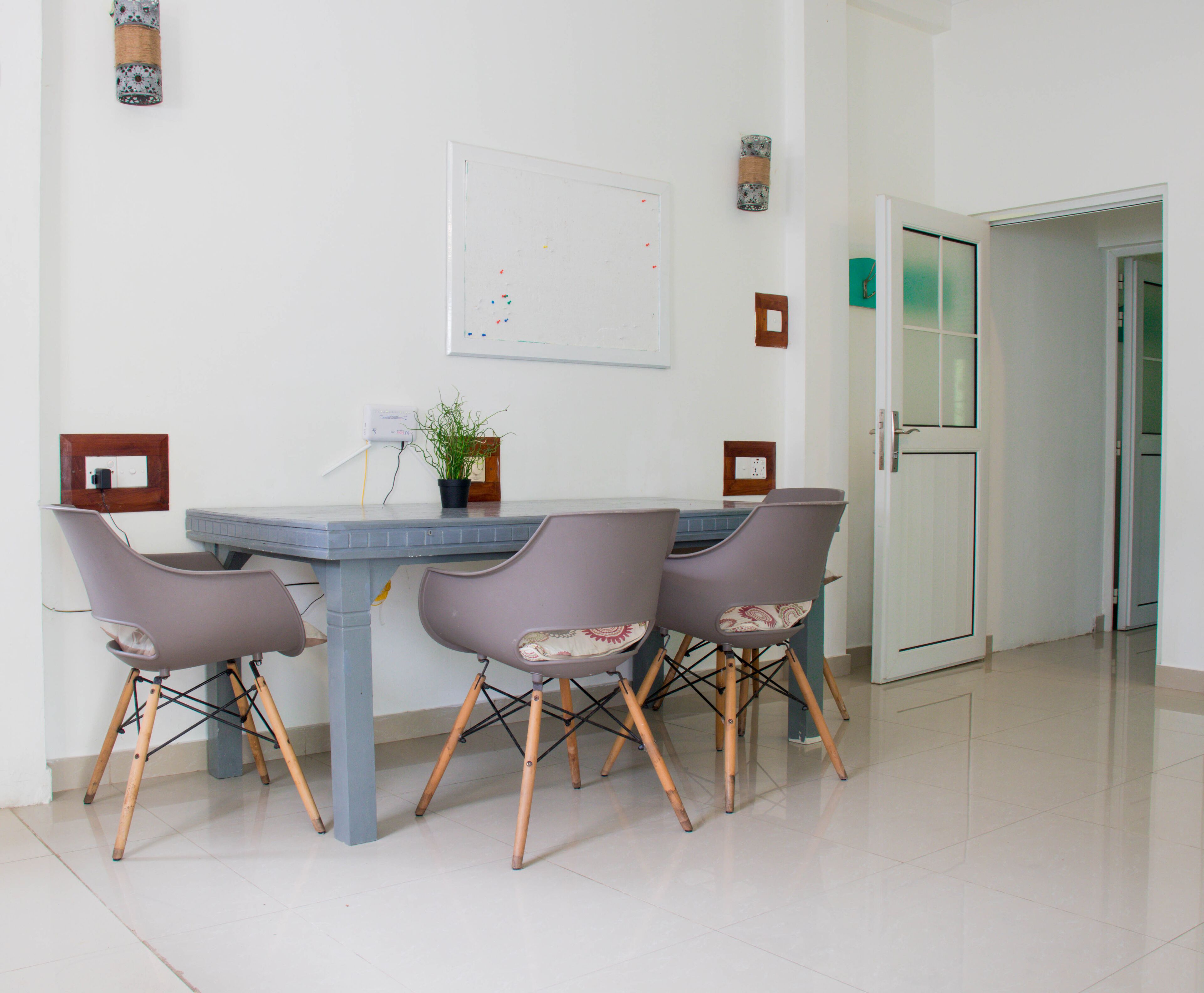 Un comedor con una mesa y cuatro sillas, una planta en maceta y una pizarra en la pared.