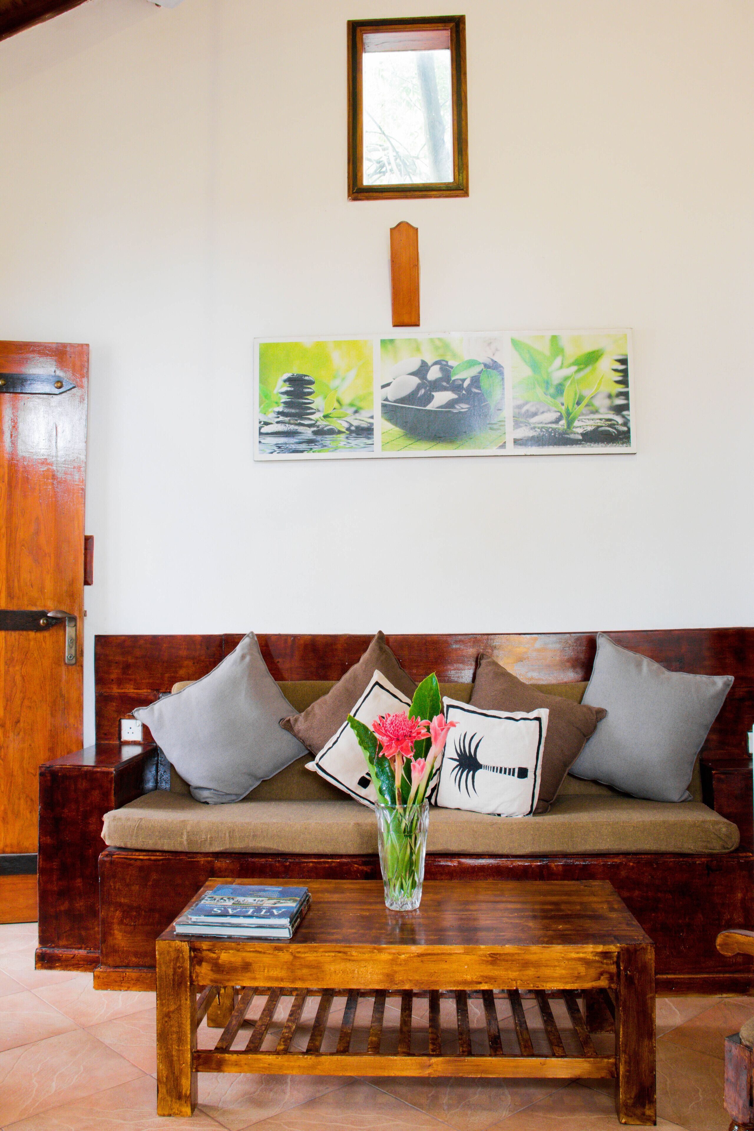 A wooden sofa with cushions, a coffee table with a book, and a vase with flowers.